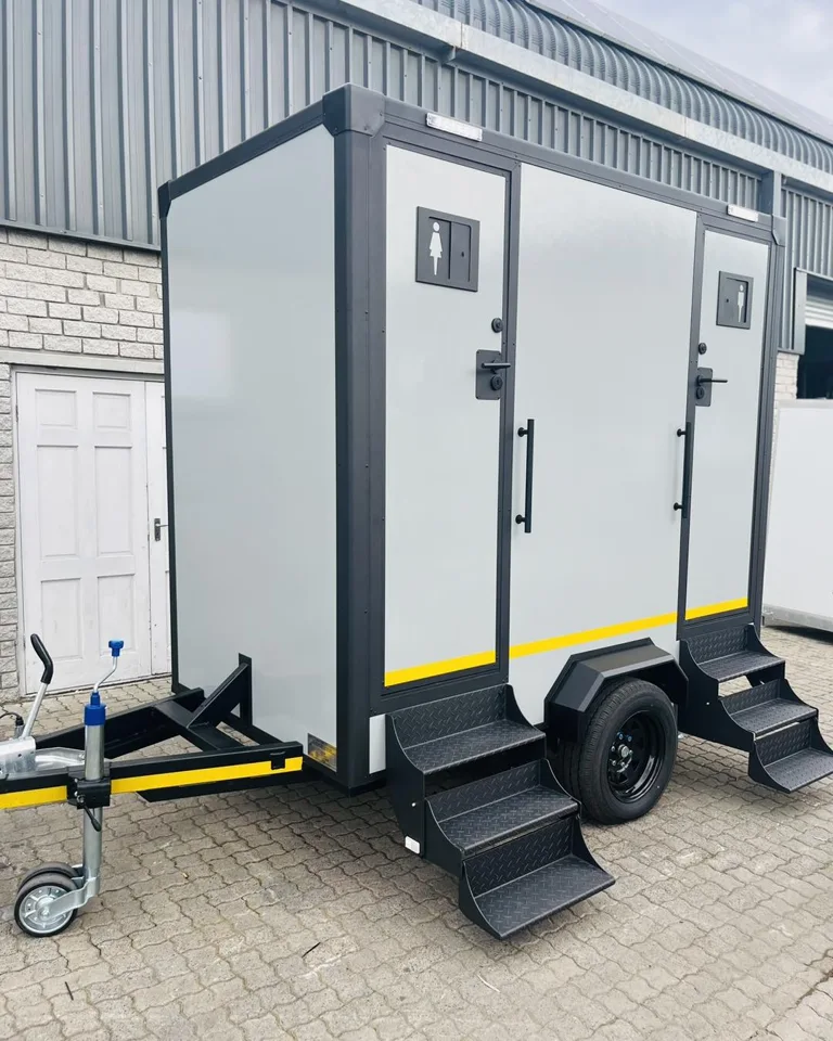Side view of a gray restroom trailer with two entrance doors