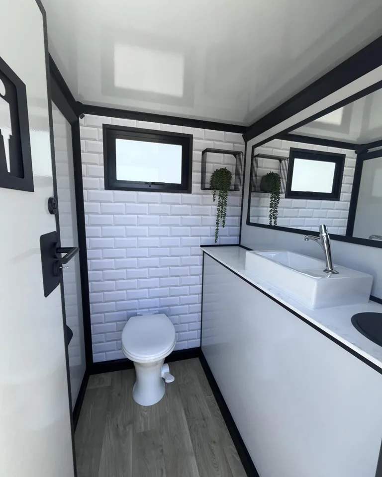 White-paneled restroom trailer interior with toilet and vanity